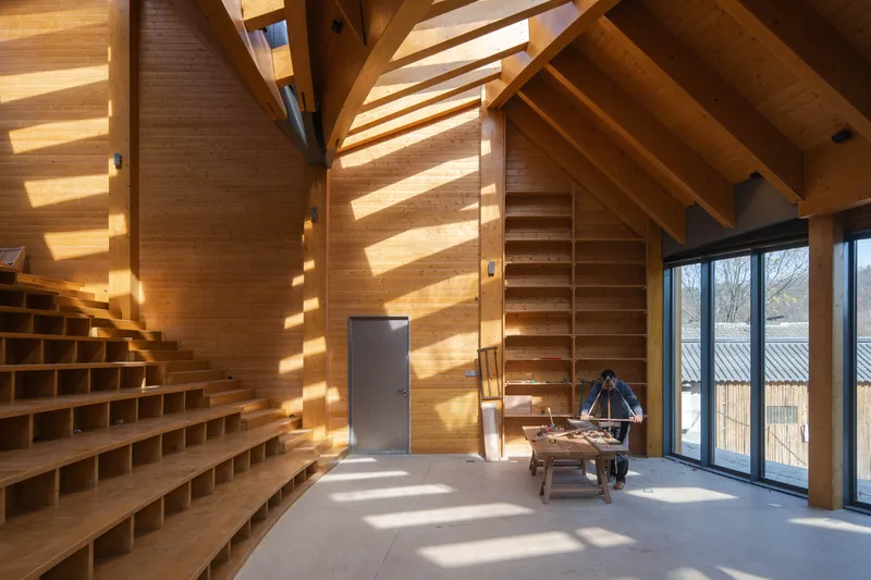 Timber-clad interior wall with integrated shelving and a person seated at a desk in sunlight