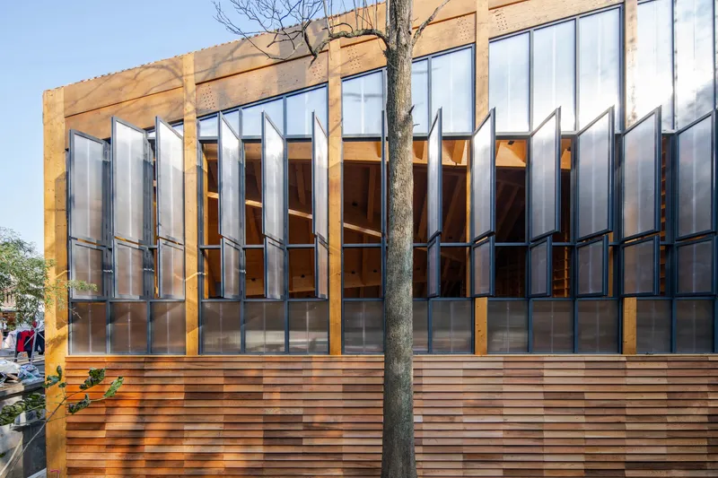 Exterior facade with vertical metal shutters above horizontal timber cladding and a bare tree in front