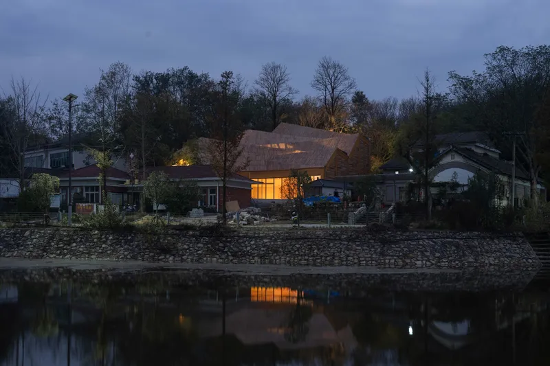 View across the water of the shingled roof structure among bare trees at dusk