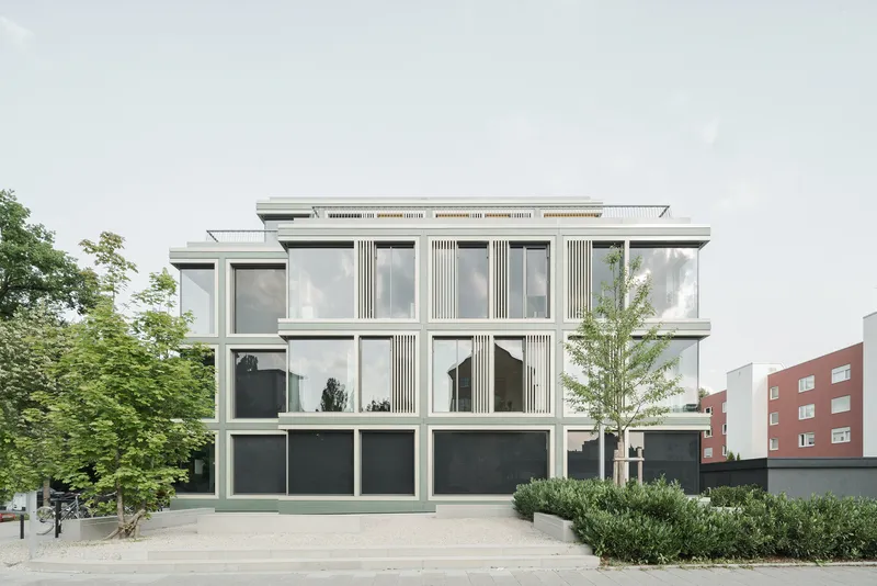 End elevation showing the modulated facade with vertical fins and dark base alongside landscaped plaza