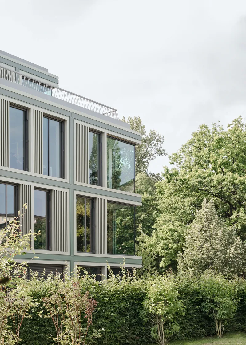 Angled view of the corner facade rising above dense shrubs and garden plantings
