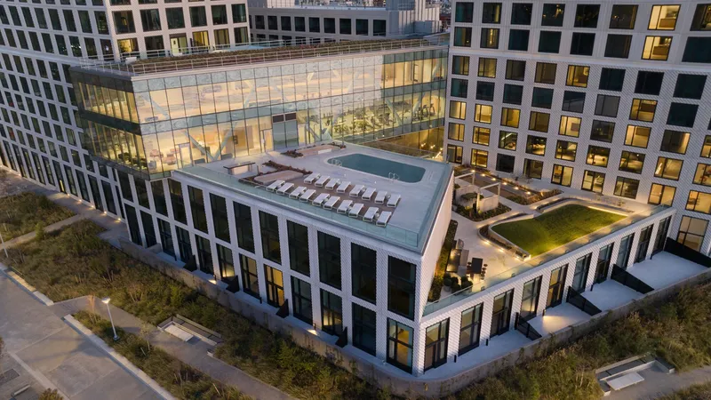 Elevated view of residential courtyard with rooftop pool and glass-enclosed amenity pavilion at twilight