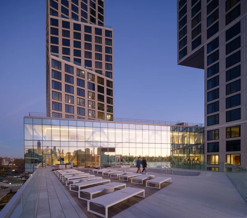 Elevated terrace with rows of timber benches facing a glass-walled pavilion at twilight
