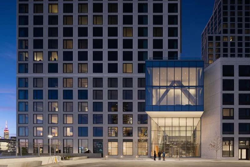 Two-story glass lobby entrance framed by gridded tower facades with pedestrians approaching at blue hour