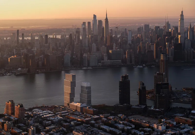 Aerial view of waterfront towers catching golden sunrise light across the river and cityscape