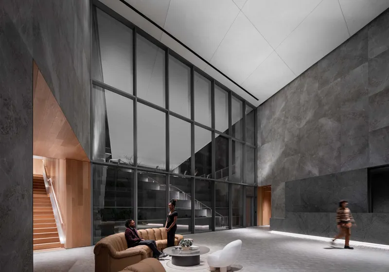 Double-height lobby with dark stone walls, curved staircase, and residents moving through diffused ceiling light