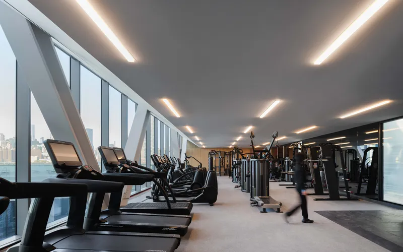 Fitness room with angled curtain wall glazing overlooking the waterfront under recessed linear ceiling lighting