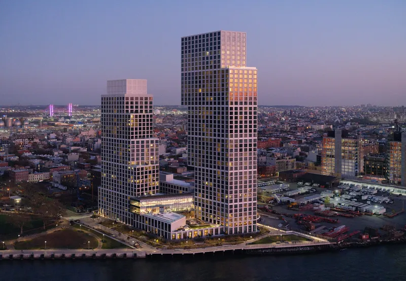 Aerial view of the stacked tower volumes at dusk with illuminated windows and distant skyline