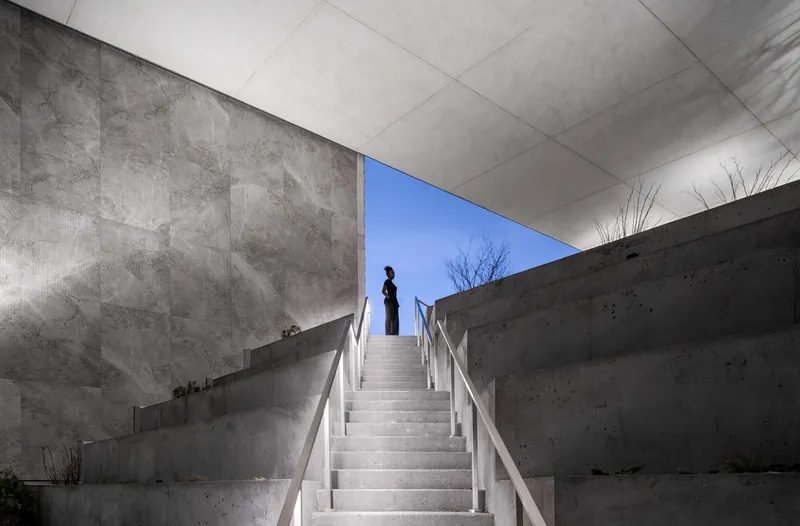 Exterior concrete staircase with metal railings ascending toward a framed opening of blue sky