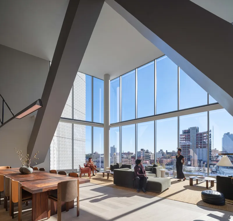 Double-height living space with angled white beams and floor-to-ceiling windows overlooking the cityscape