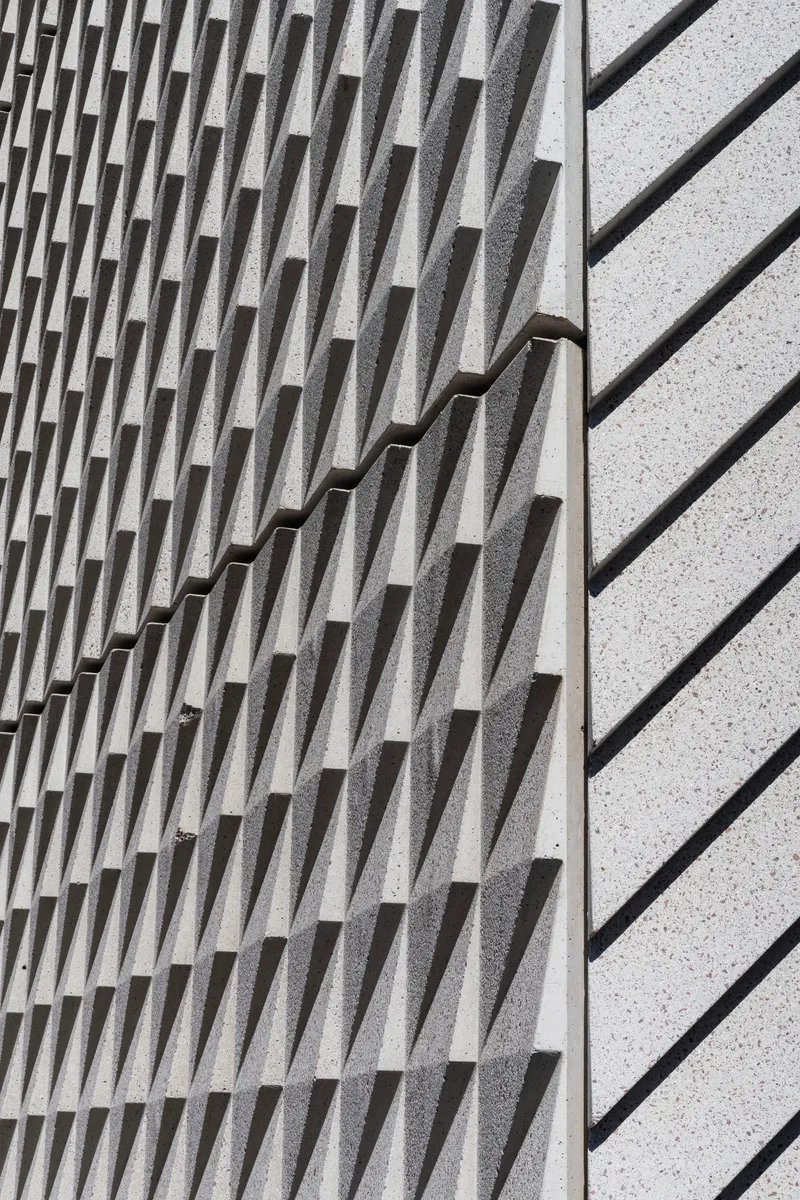 Close-up of textured concrete wall with protruding vertical fins meeting a smooth terrazzo surface
