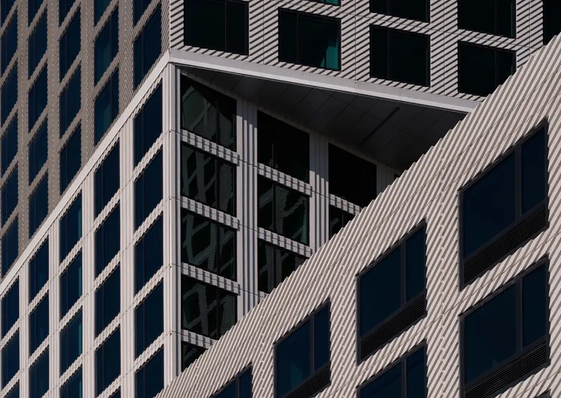 Facade detail showing recessed balcony framed by diagonal striped cladding and dark glazing