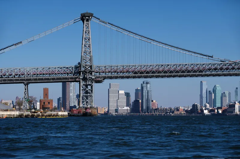View of the white grid tower facades from across the river beneath an industrial cable-stayed bridge