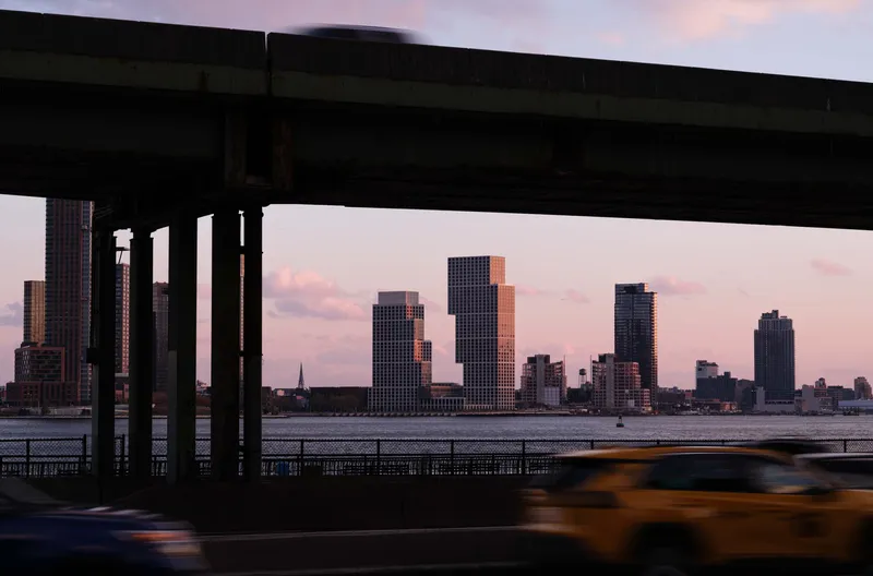 View beneath an elevated highway of the stepped towers across the water at dusk with a taxi passing