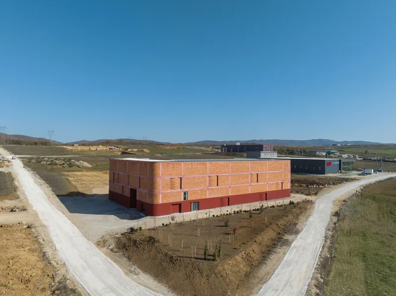 Aerial view of the terracotta brick volume with gridded facade in a rural landscape under clear sky