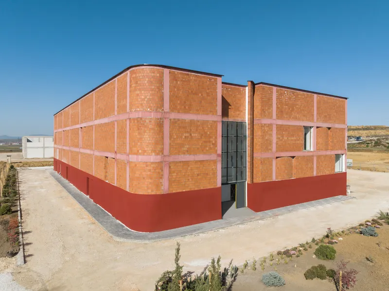 Corner view showing glazed entry slot between terracotta brick bays with exposed structural grid