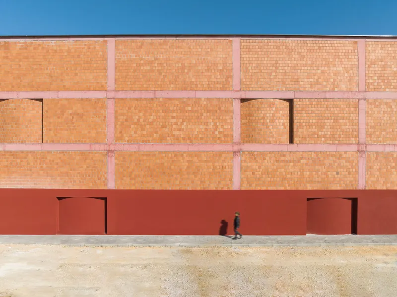 Facade with two doorways in red plaster base below upper terracotta brick wall as figure walks past