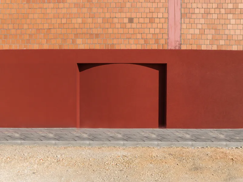 Arched doorway recessed into the red plaster wall above a patterned stone paving strip