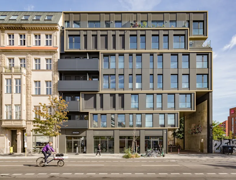 Street view of the gridded facade with ribbon windows and balconies as a cyclist passes by