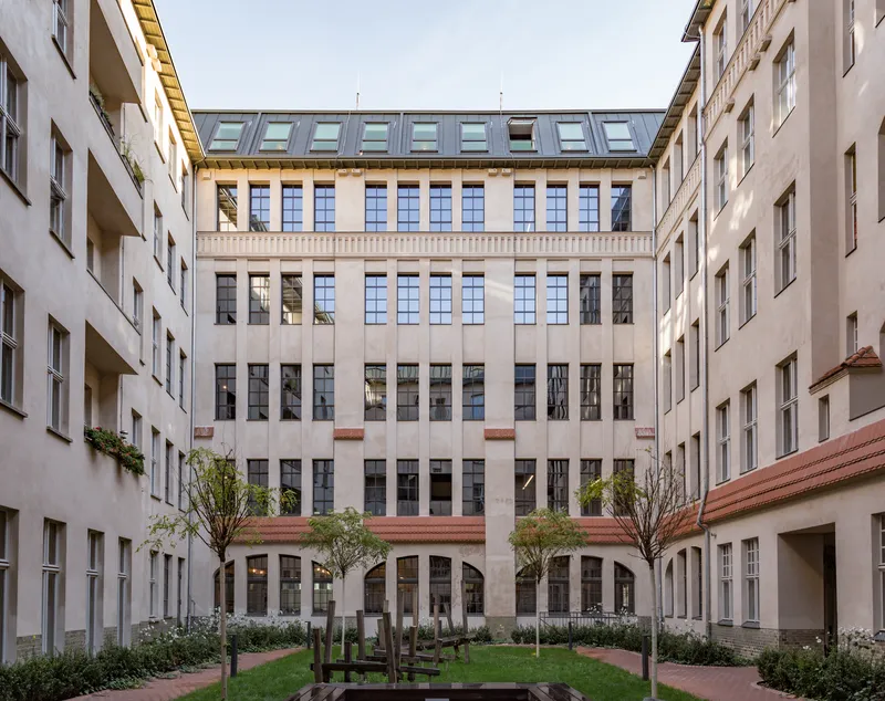 Courtyard view framed by flanking residential wings with young trees and planted beds on brick pavers