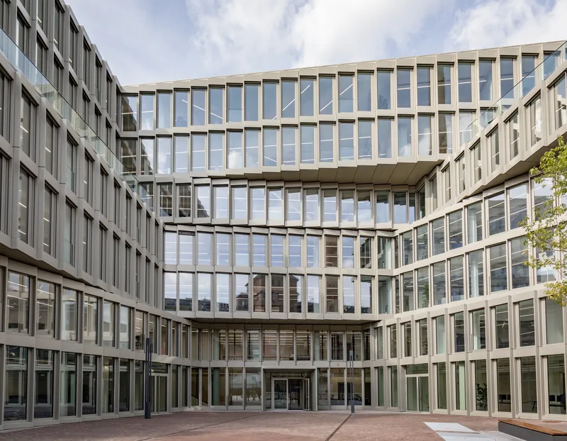 Glazed courtyard facade with cantilevered upper floors and vertical white framing under partly cloudy skies