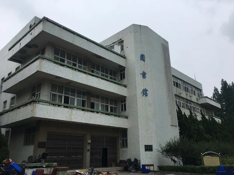 Three-story concrete facade with terrazzo cladding and vertically fluted tower element under overcast sky