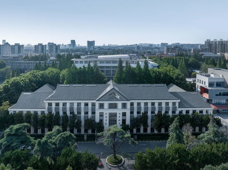 Aerial view of the white symmetrical facade with central pediment surrounded by dense green trees