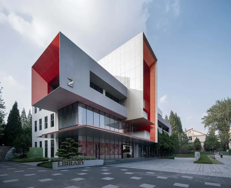 Street view of the cantilevered volume clad in red and grey panels above a glazed ground floor