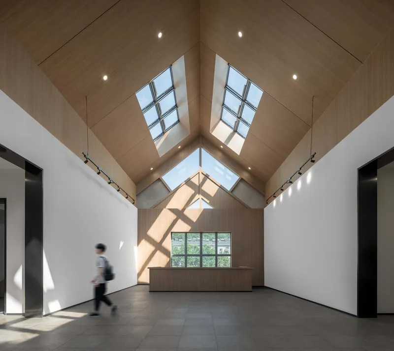Vaulted gallery space with wood ceiling, skylight ridge and a figure passing through sunlight