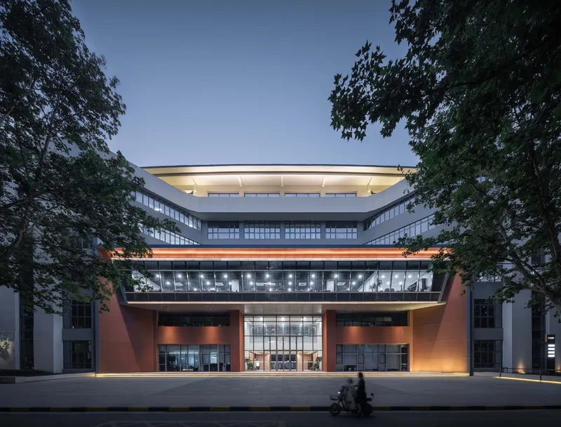 Illuminated entrance facade at dusk with red angled columns flanking the glazed lobby