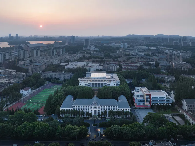 Aerial campus view at sunset showing the original symmetrical building and new tiered library volume