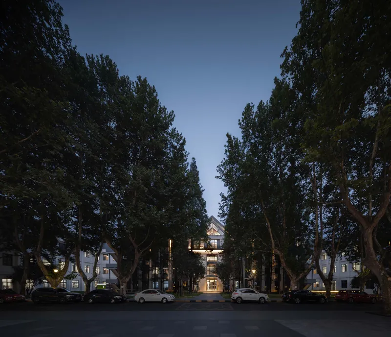 Illuminated central building framed by mature trees and parked cars in evening light