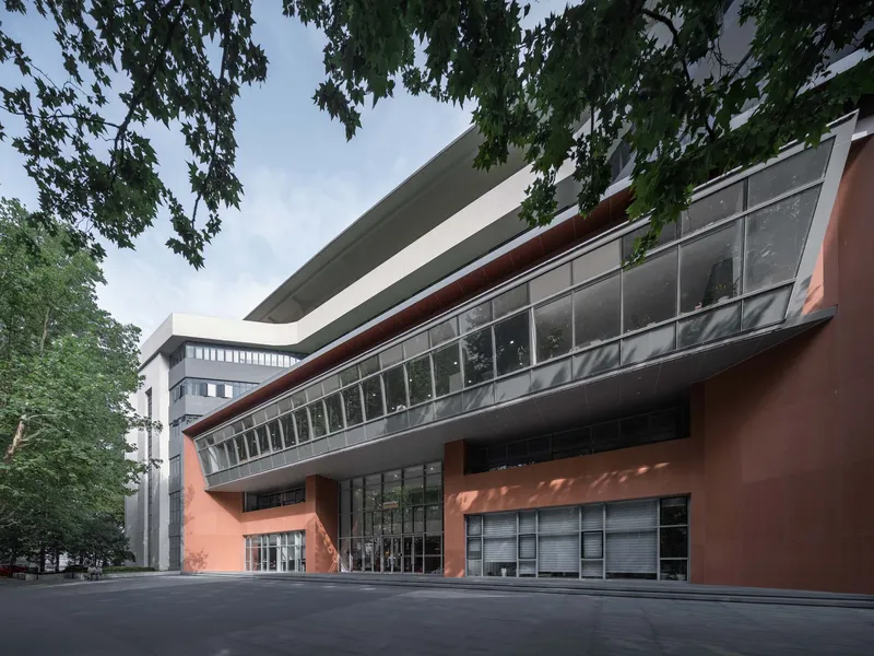Curved facade with horizontal glazing bands and terracotta panels beneath overhanging tree branches