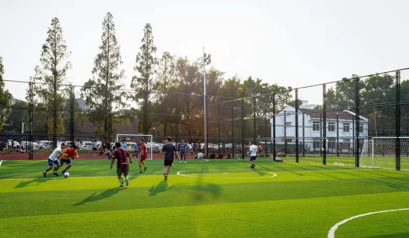 Synthetic turf sports pitch with mesh fencing and players in afternoon light