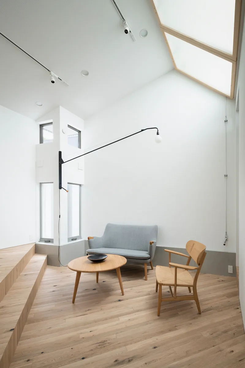 Double-height living room with timber-framed skylights and a grey sofa beneath tall windows
