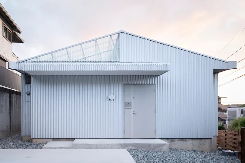 Street view of the white corrugated metal facade with a central door and translucent roof panels
