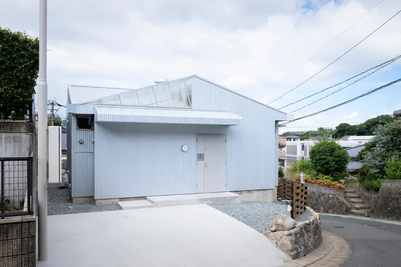 Corner view showing the corrugated metal volume with gravel courtyard and residential neighborhood context
