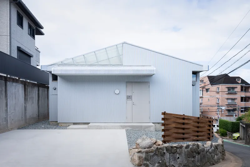White corrugated metal facade with gabled roof and clerestory windows facing a gravel courtyard