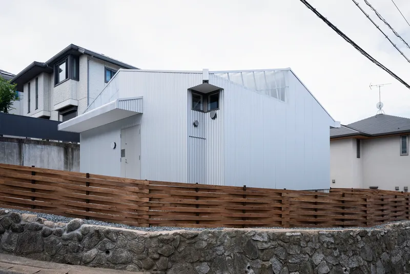 Horizontal timber slat fence atop a stone retaining wall with the corrugated house beyond