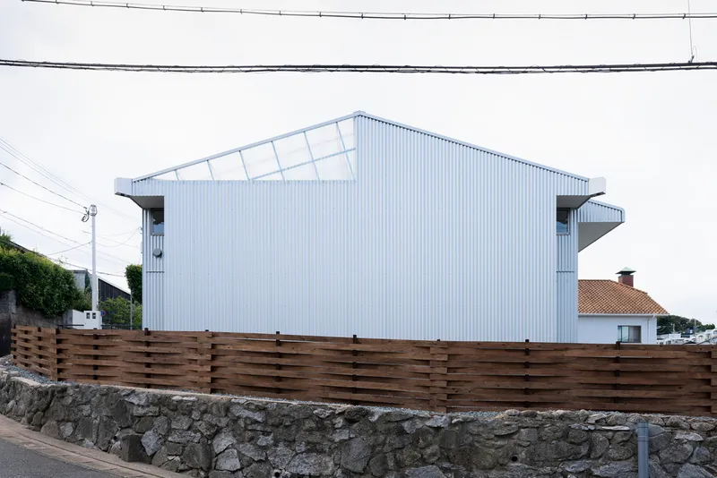 Street view of the gabled house with translucent clerestory panels and overhead power lines