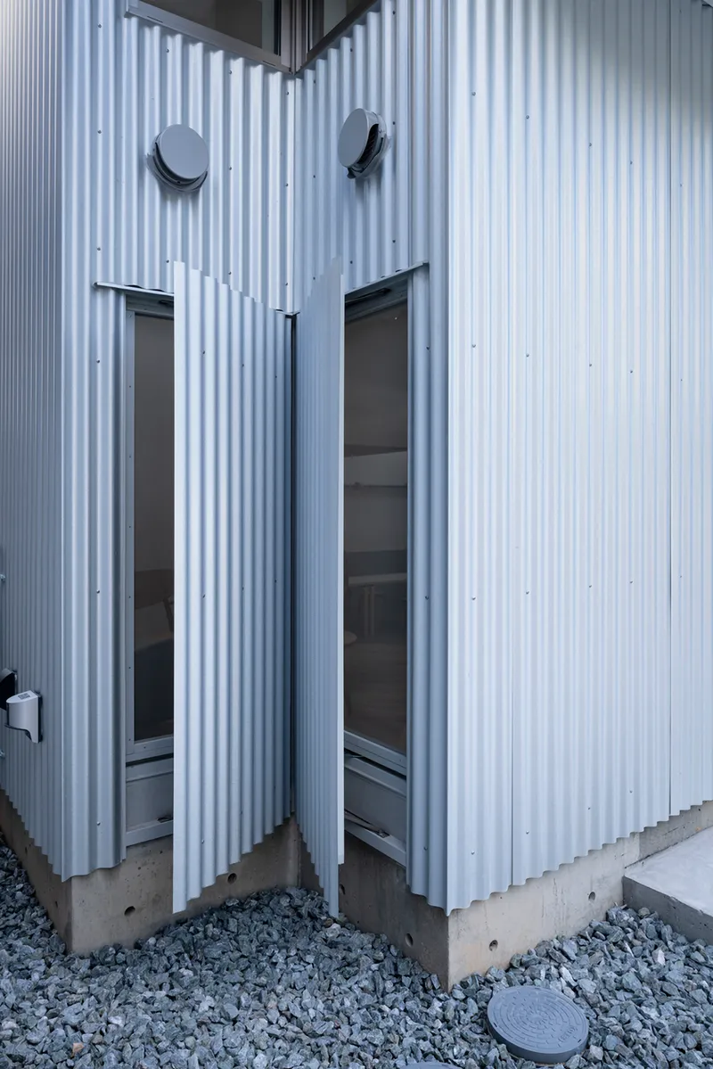 Corner detail of the corrugated metal cladding with glazed door openings and exposed concrete base