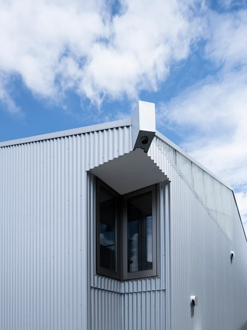 Projecting window box with metal hood and white chimney against blue sky with clouds