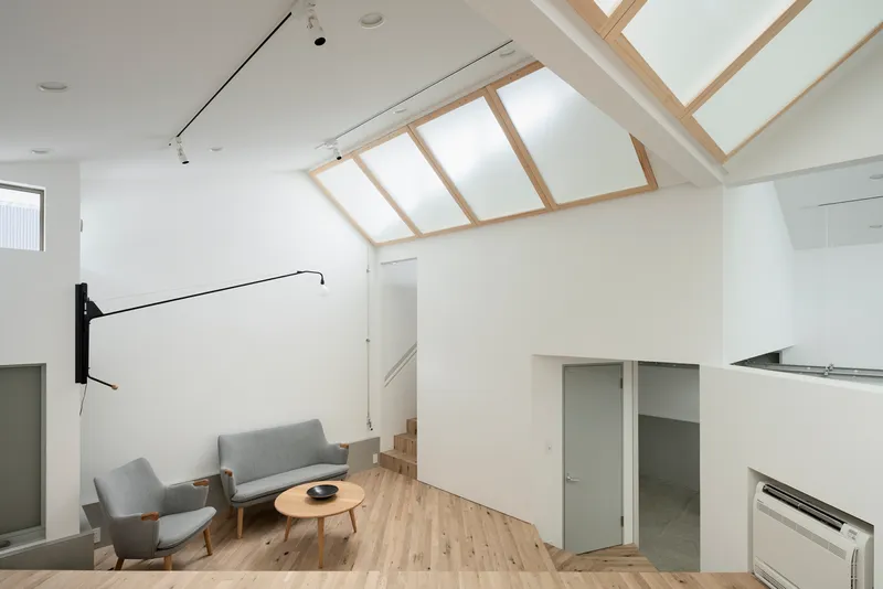 Double-height living space with timber-framed skylights and grey upholstered seating on wood flooring