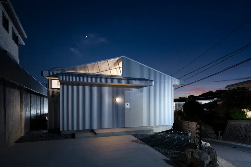 Street view of the vertical corrugated cladding and glowing clerestory windows under a crescent moon