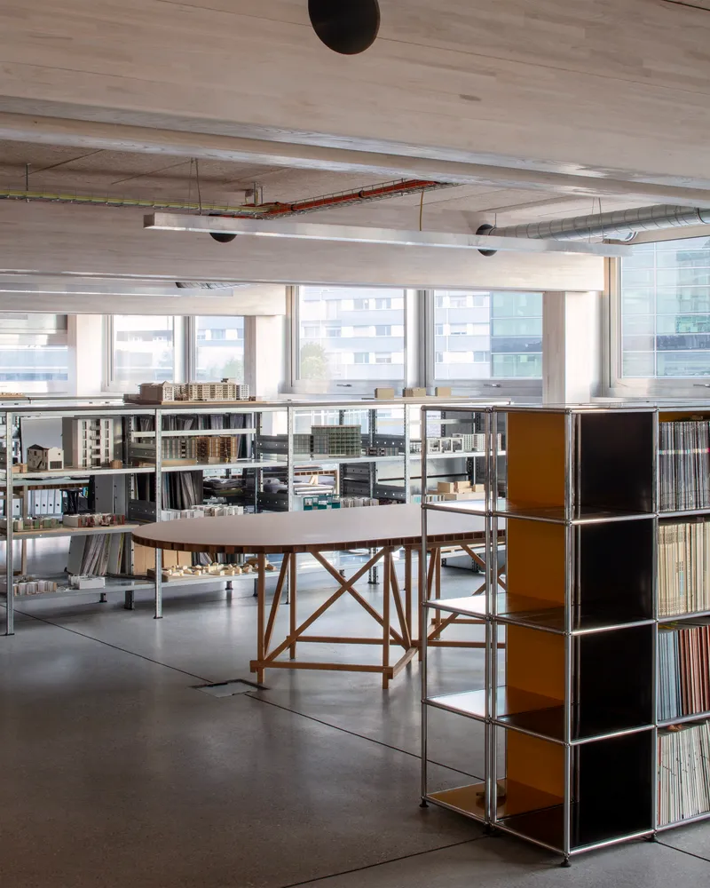 Open-plan studio with exposed concrete ceiling, modular shelving and timber trestle work table