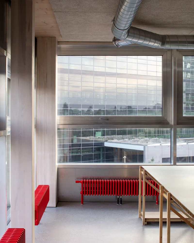 Interior space with exposed concrete ceiling, spiral ductwork and red radiators beneath full-height glazing
