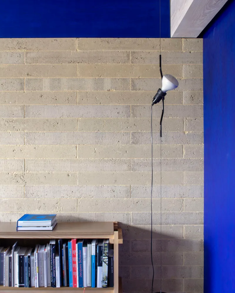 Concrete block wall with low bookshelf and articulated wall lamp against a blue painted surface