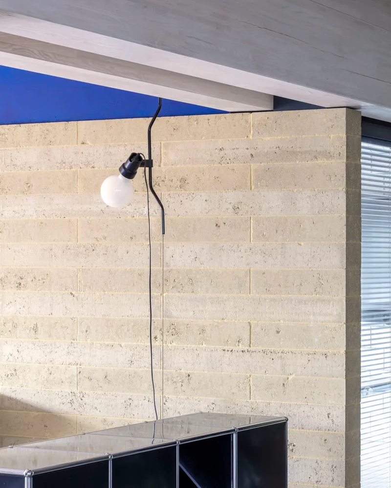 Wall-mounted lamp with exposed cord on concrete block wall beneath a timber ceiling