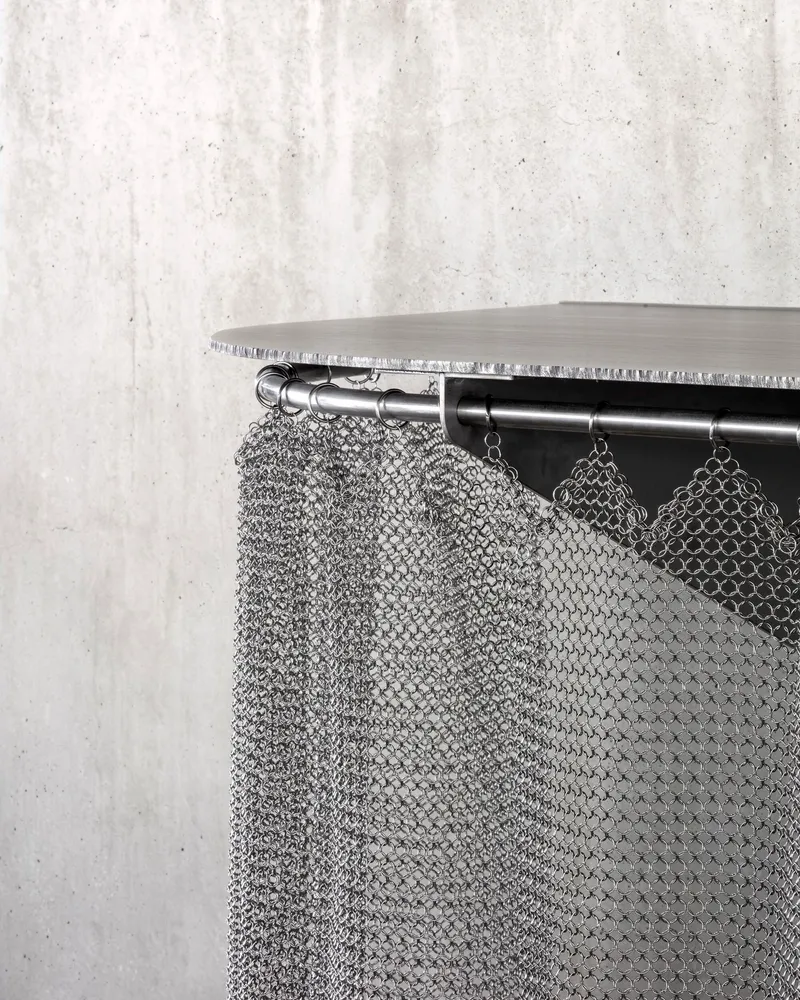 Close-up of chainmail curtain hanging from steel rod beneath a timber shelf edge
