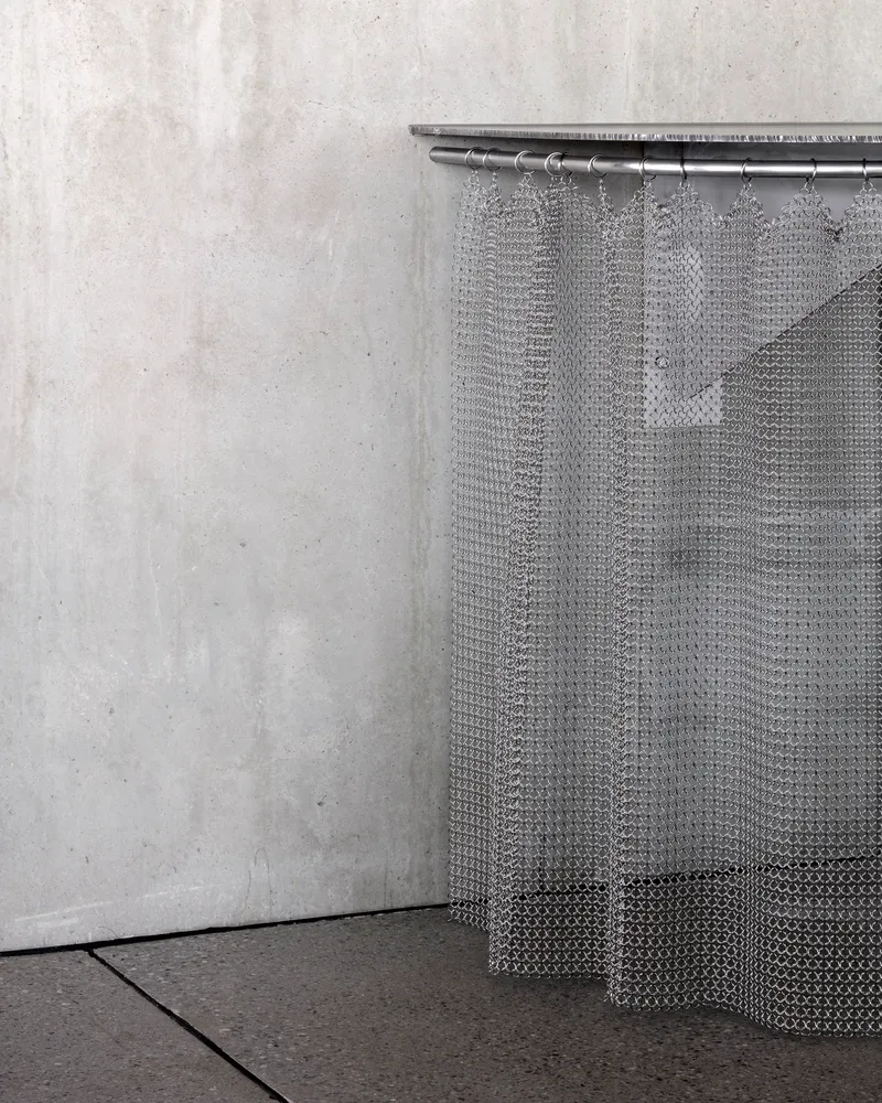 Metal mesh curtain suspended from rod in corner against poured concrete wall